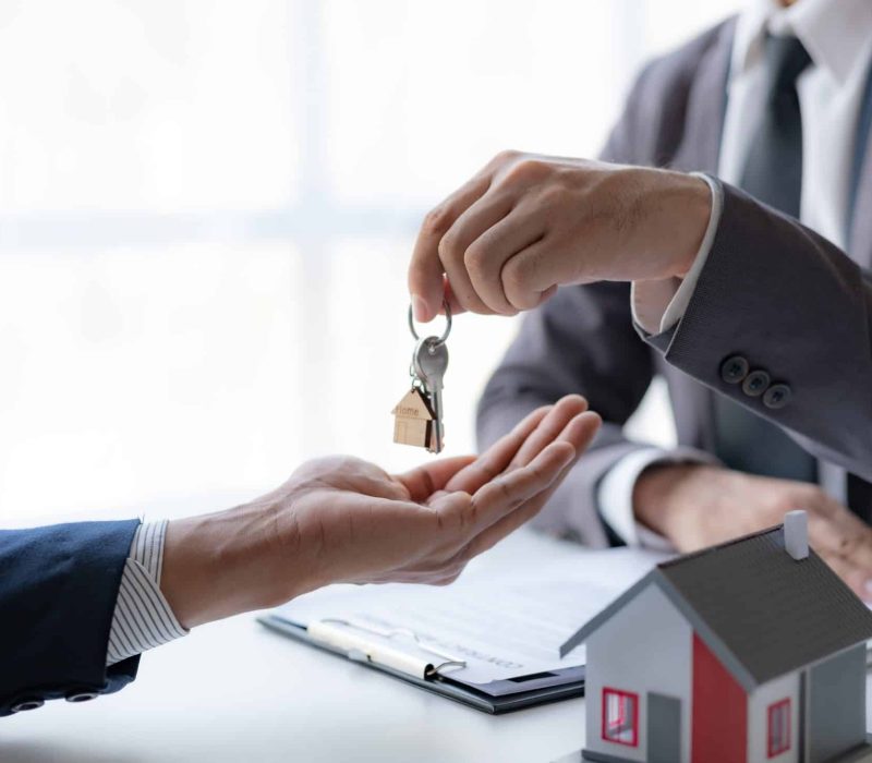 A professional real estate agent is giving house keys to a client during a property sale transaction.